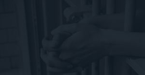 Dark view of hands hanging on prison bars
